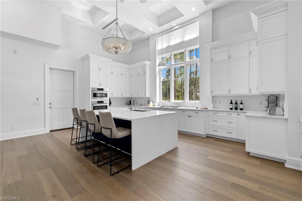 Kitchen with a towering ceiling, a center island with sink, light stone counters, light wood finished floors, and a breakfast bar area