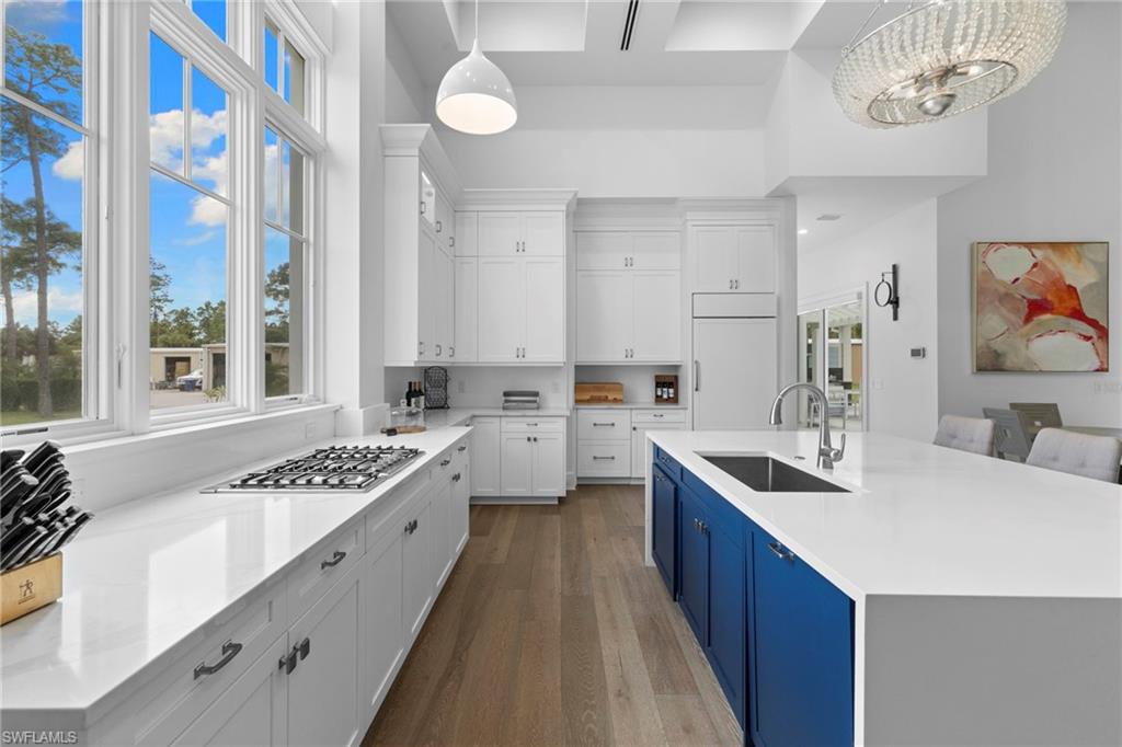 Kitchen with white cabinetry, light stone counters, dark wood-style flooring, a center island with sink, and hanging light fixtures