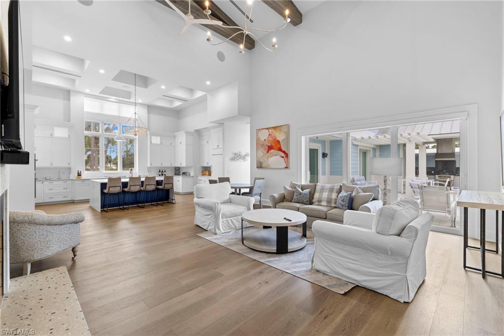 Living room featuring light wood finished floors, a chandelier, a high ceiling, and beam ceiling