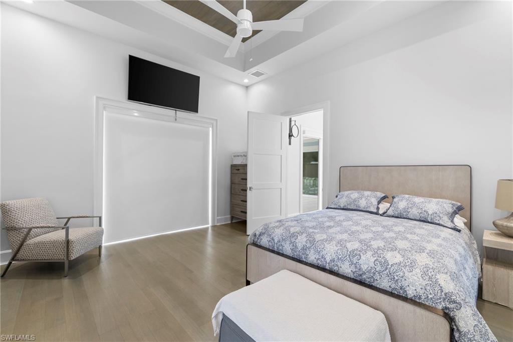 Bedroom featuring light wood-type flooring, a ceiling fan, a high ceiling, a tray ceiling, and recessed lighting