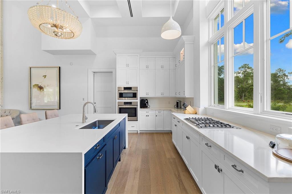 Kitchen featuring white cabinetry, light wood-type flooring, light stone counters, a center island with sink, and a high ceiling