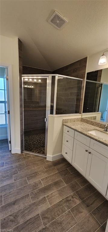 Full bath featuring vanity, wood finish floors, a stall shower, and vaulted ceiling