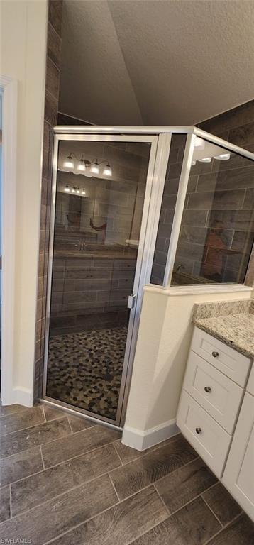 Bathroom featuring wood finish floors, a shower stall, vanity, and a textured ceiling