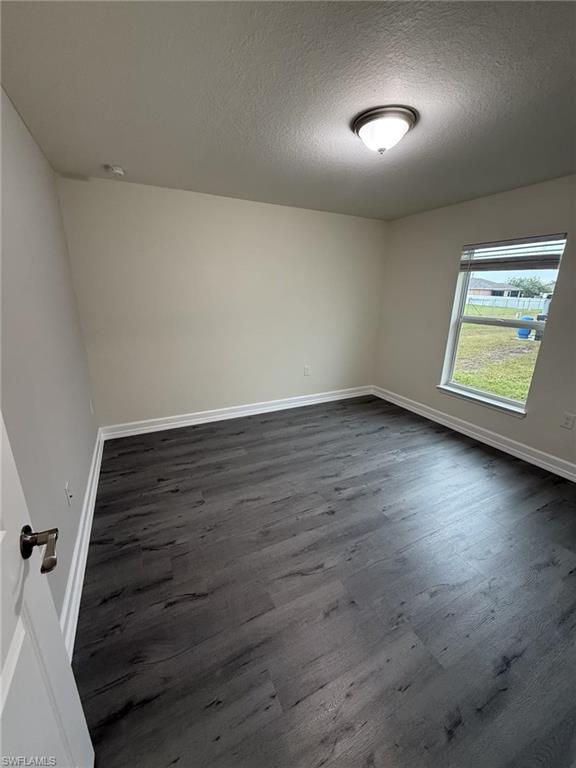 Unfurnished room featuring dark wood-type flooring and a textured ceiling