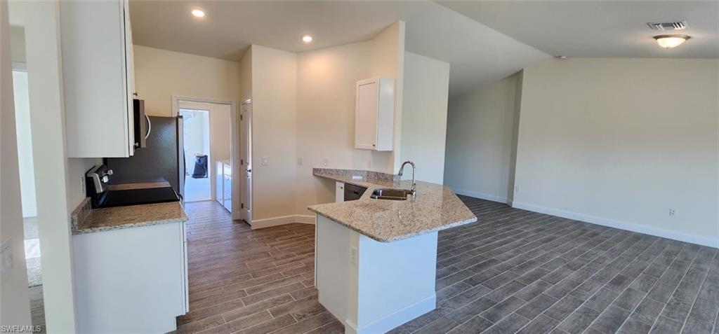 Kitchen featuring light stone countertops, white cabinets, a peninsula, wood tiled floors, and stainless steel appliances