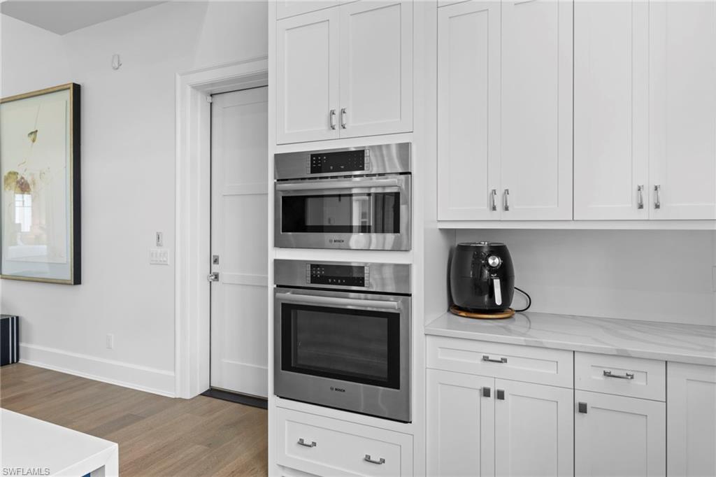 Kitchen featuring white cabinetry, light stone counters, light wood-type flooring, and double oven