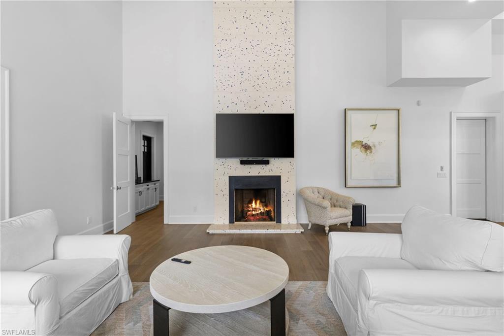 Living area featuring a towering ceiling, a warm lit fireplace, and wood finished floors