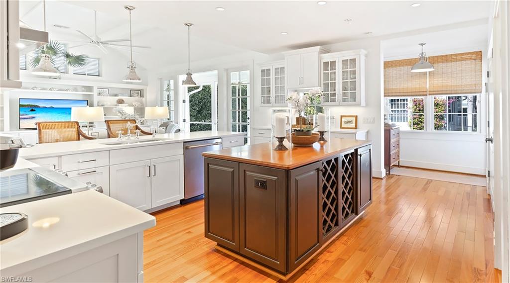 Two tone kitchen with decorative light fixtures, light wood finished floors, glass insert cabinets, stainless steel dishwasher, and healthy amount of natural light