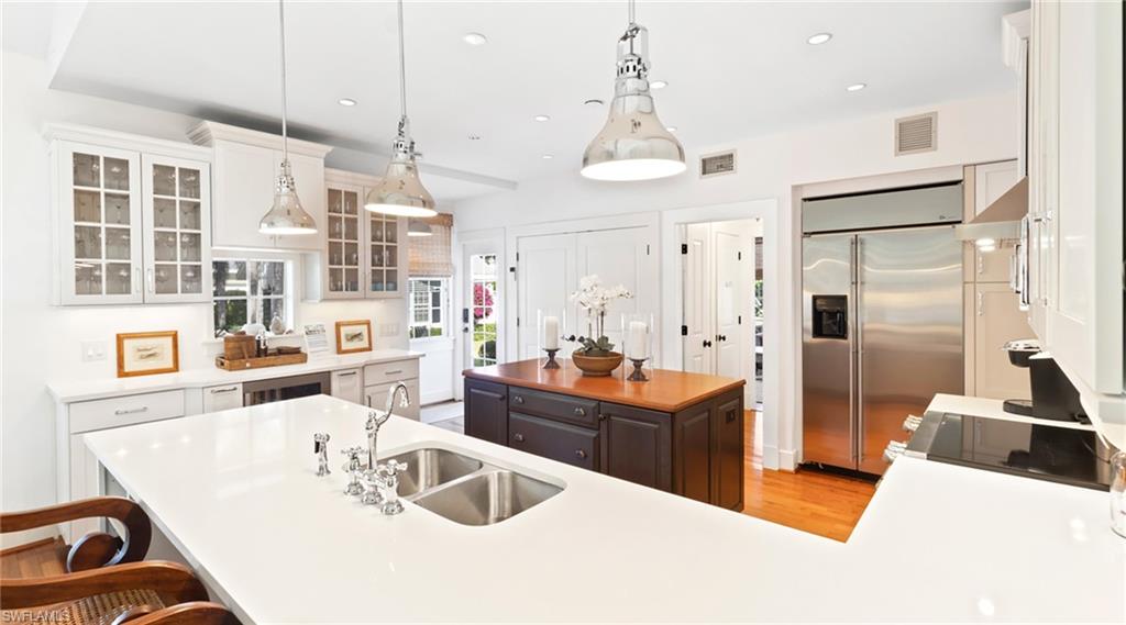 Kitchen with a kitchen island, glass insert cabinets, stainless steel built in refrigerator, a breakfast bar area, and hanging light fixtures