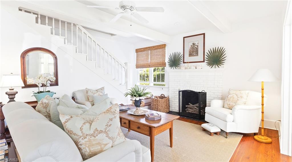 Living area featuring wood finished floors, a ceiling fan, a fireplace, and beam ceiling