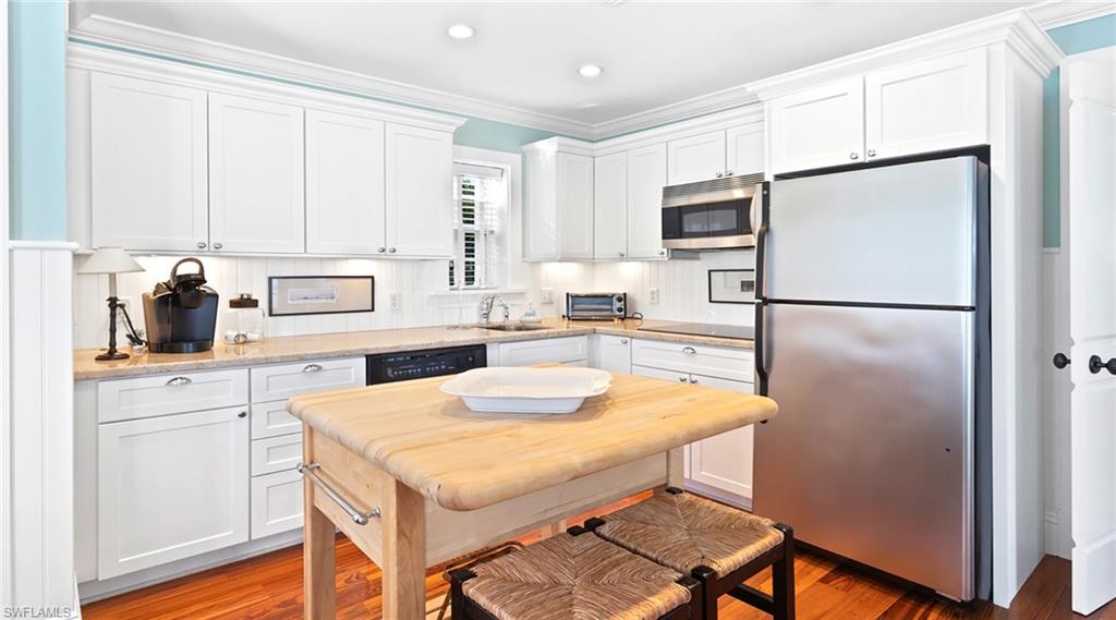 Kitchen with ornamental molding, stainless steel appliances, white cabinets, light wood-type flooring, and light stone countertops