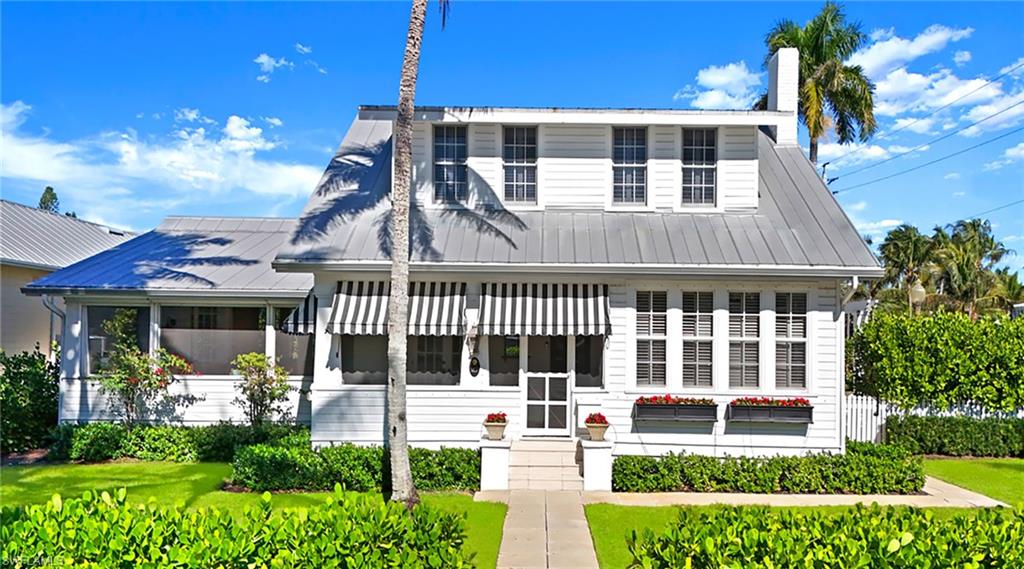 View of front of home with a metal roof, a sunroom, a chimney, a front yard, and entry steps