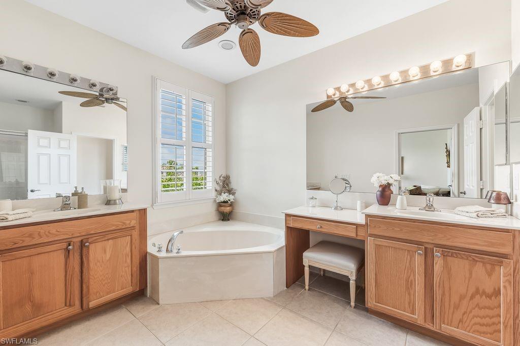 Master Bathroom with a soaking tub bath, two vanities, light tile patterned floors, walk-in shower, ceiling fan, and plantation shutters