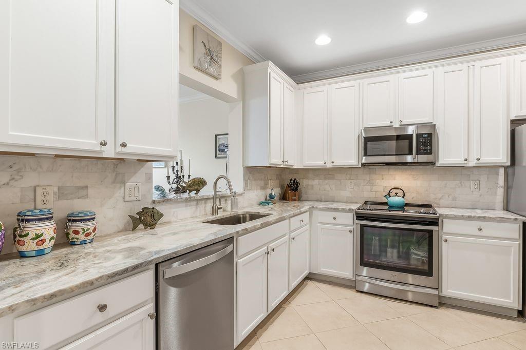 Kitchen featuring appliances with stainless steel finishes, sleek white cabinetry, light tile patterned floors, ornamental molding, and light granite counters and backsplash