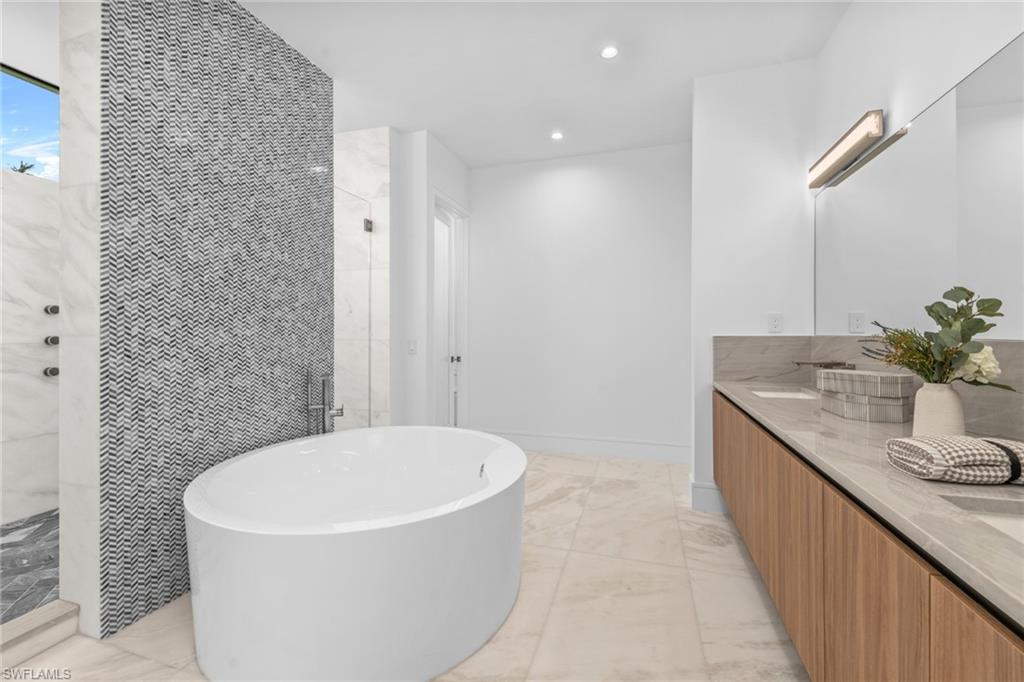 Master Bathroom featuring light marble finish flooring, tiled shower, a freestanding tub, double vanity, and recessed lighting