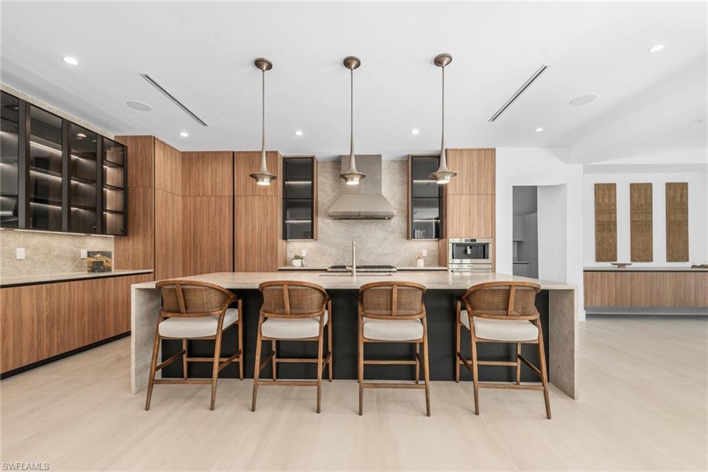 Kitchen with light stone counters, glass insert cabinets, a large island, a kitchen breakfast bar, and recessed lighting
