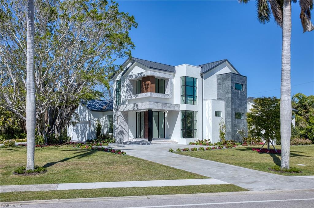 Modern home with a front yard, stucco siding, a metal roof, a balcony, and covered porch