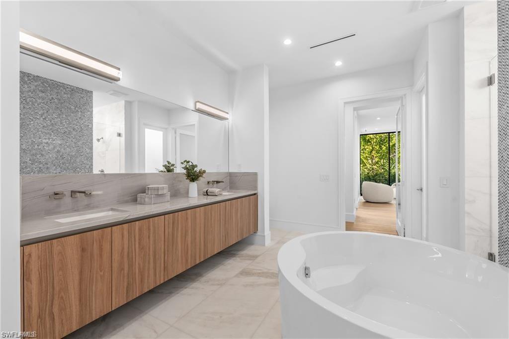 Full bathroom with a shower stall, double vanity, recessed lighting, a freestanding tub, and light marble finish flooring