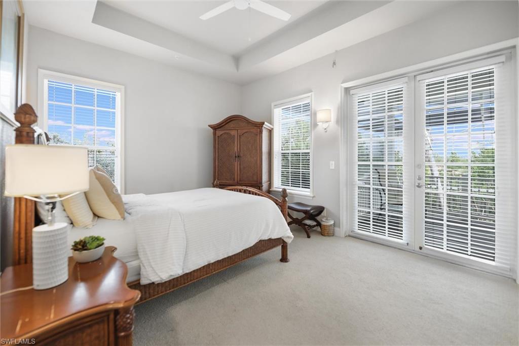 Carpeted bedroom featuring access to outside, multiple windows, a tray ceiling, and ceiling fan