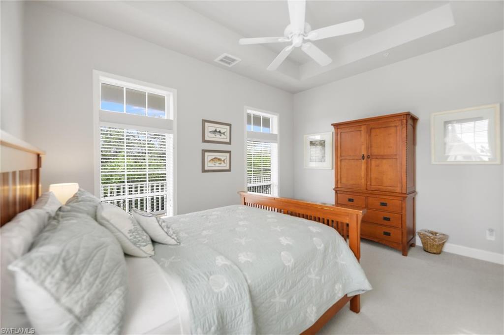 Bedroom with light carpet, a raised ceiling, and a ceiling fan