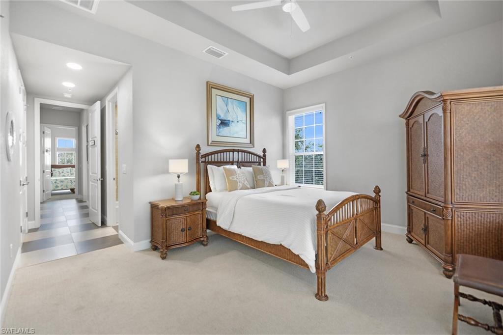 Bedroom featuring light carpet, multiple windows, a ceiling fan, and a raised ceiling