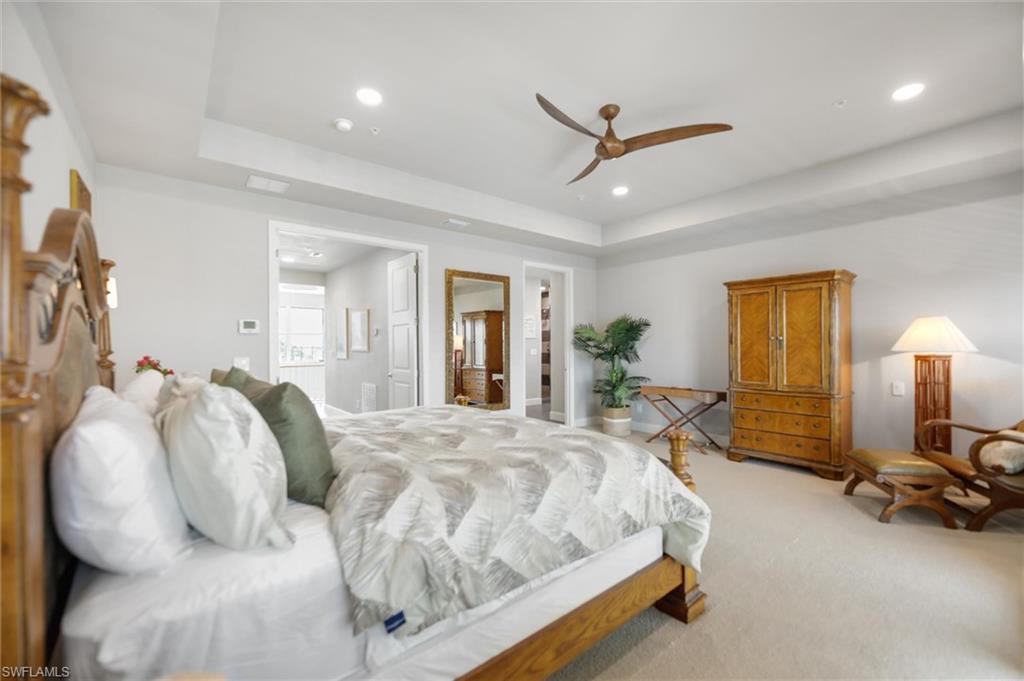 Bedroom with a raised ceiling, light colored carpet, recessed lighting, ceiling fan, and ensuite bath