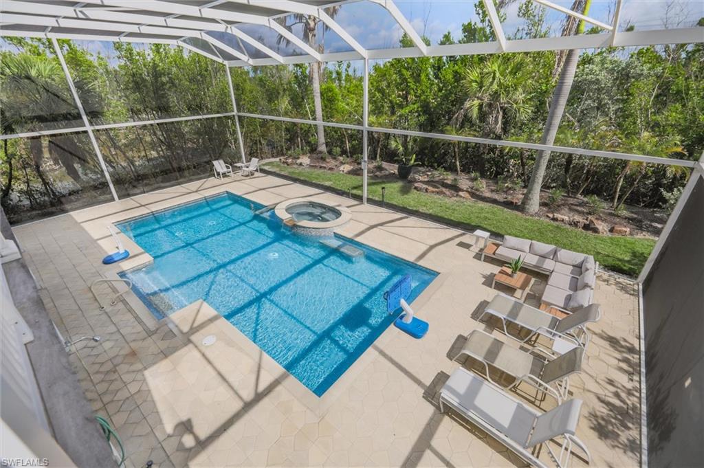 View of pool with a patio, glass enclosure, a pool with connected hot tub, and view of wooded area