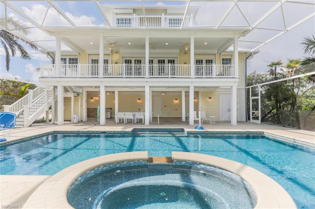 Back of property with a patio area, a lanai, a pool with connected hot tub, stairway, and a balcony