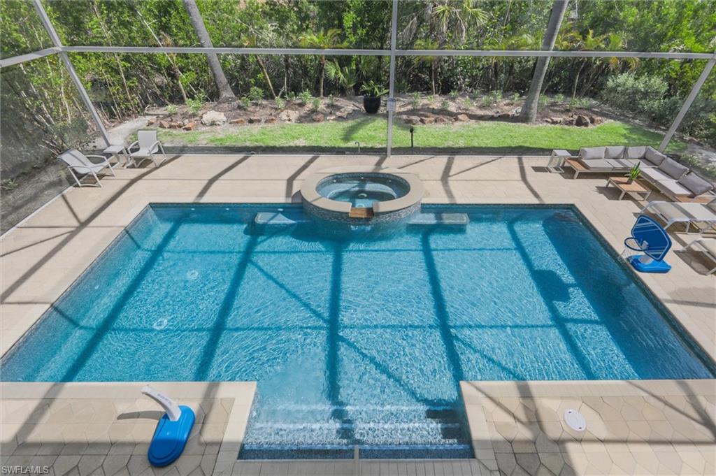 View of pool featuring glass enclosure, a pool with connected hot tub, and a patio area