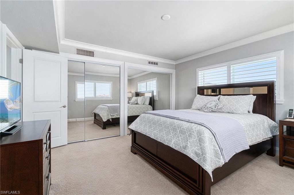 Bedroom with two closets, ornamental molding, and light carpet