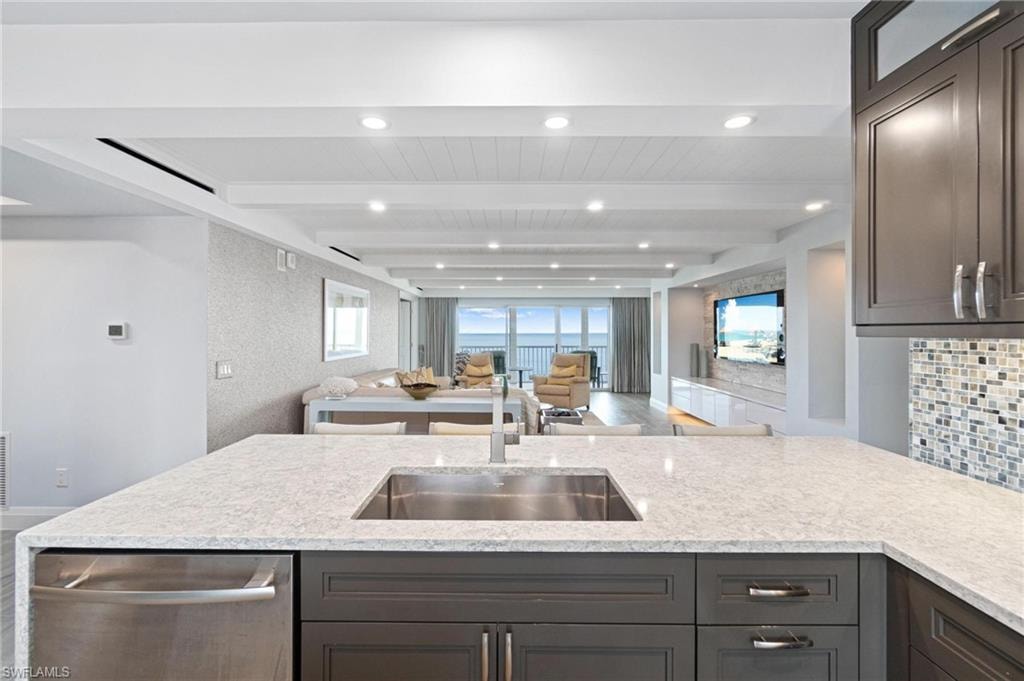 Kitchen with light stone countertops, stainless steel dishwasher, open floor plan, recessed lighting, and dark brown cabinetry