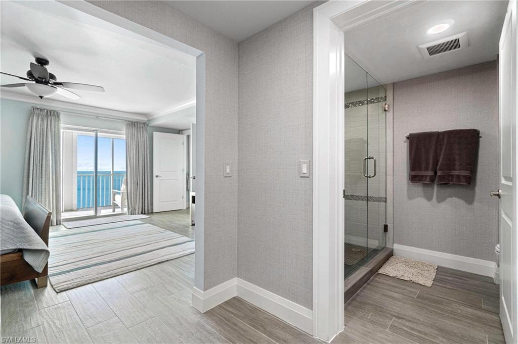 Bathroom featuring light wood-style floors, a shower stall, ceiling fan, and a water view