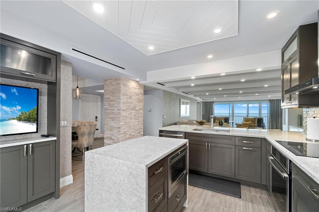 Kitchen featuring open floor plan, light stone countertops, stainless steel appliances, light wood-style floors, and a peninsula