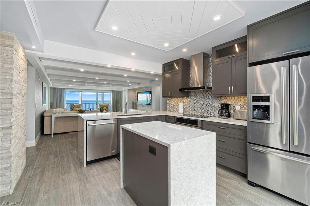 Kitchen featuring appliances with stainless steel finishes, a peninsula, open floor plan, light stone countertops, and glass insert cabinets