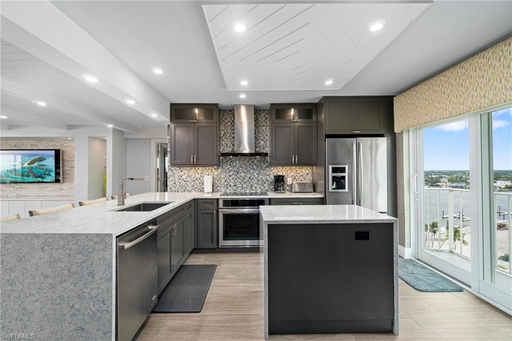 Kitchen featuring light stone counters, backsplash, appliances with stainless steel finishes, a peninsula, and a kitchen island