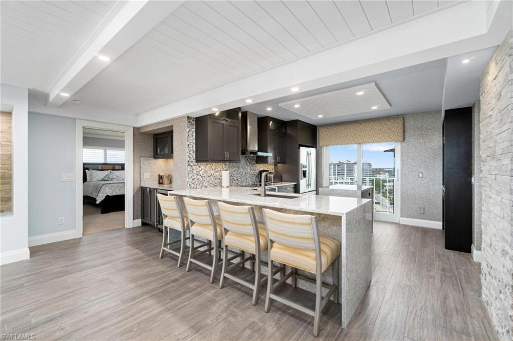Kitchen featuring a peninsula, light stone countertops, healthy amount of natural light, a kitchen breakfast bar, and beam ceiling