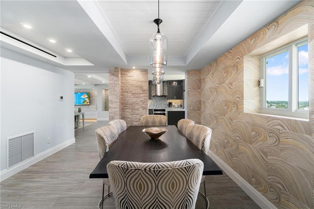 Dining area featuring a raised ceiling, wood finished floors, wallpapered walls, and recessed lighting