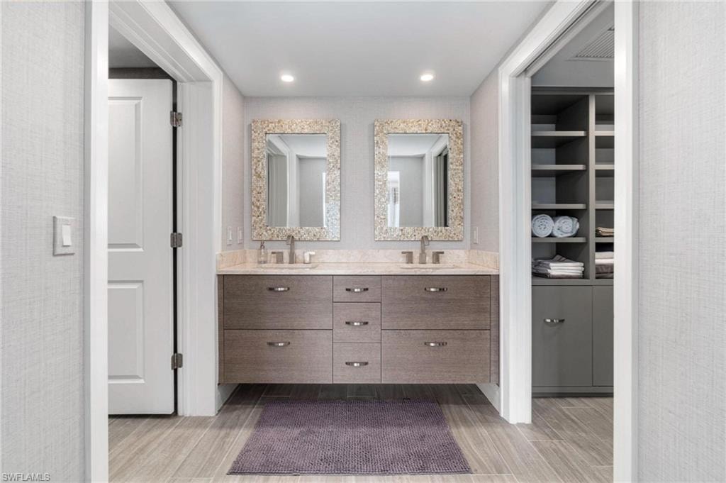 Full bath with double vanity, light wood finished floors, and recessed lighting