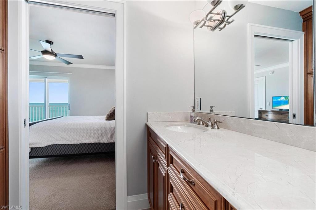 Ensuite bathroom featuring vanity, crown molding, carpet, and ceiling fan