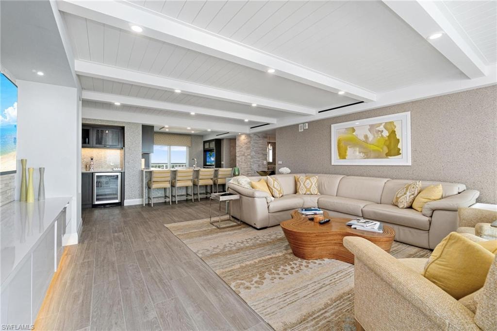 Living room with beam ceiling, beverage cooler, wood finished floors, bar with sink, and recessed lighting