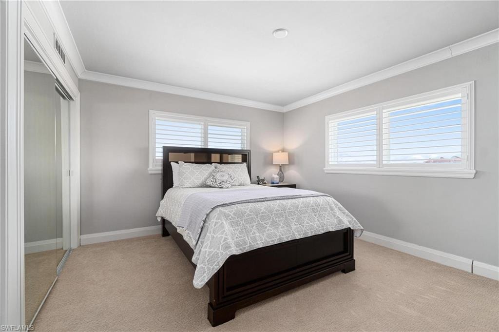 Bedroom with a closet, crown molding, and light colored carpet