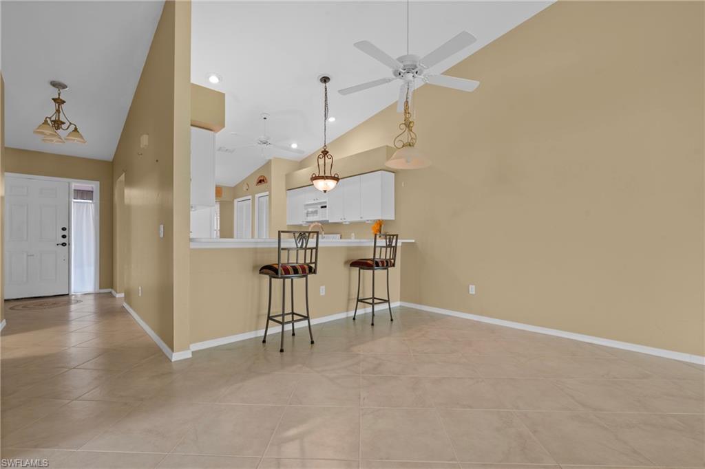 Open concept living area featuring vaulted ceilings, tile flooring, a breakfast bar, and a ceiling fan