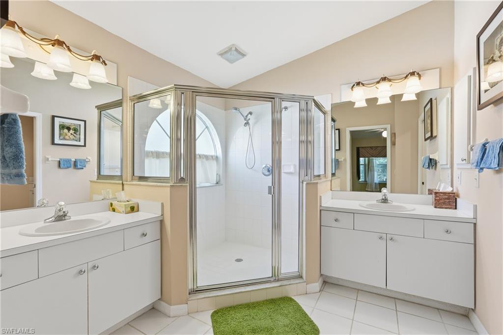 Full bath with light tile patterned floors, a shower stall, lofted ceiling, two vanities, and healthy amount of natural light