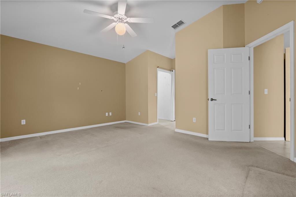 Spacious room featuring vaulted ceilings, light-toned carpeting, and a ceiling fan with integrated lighting