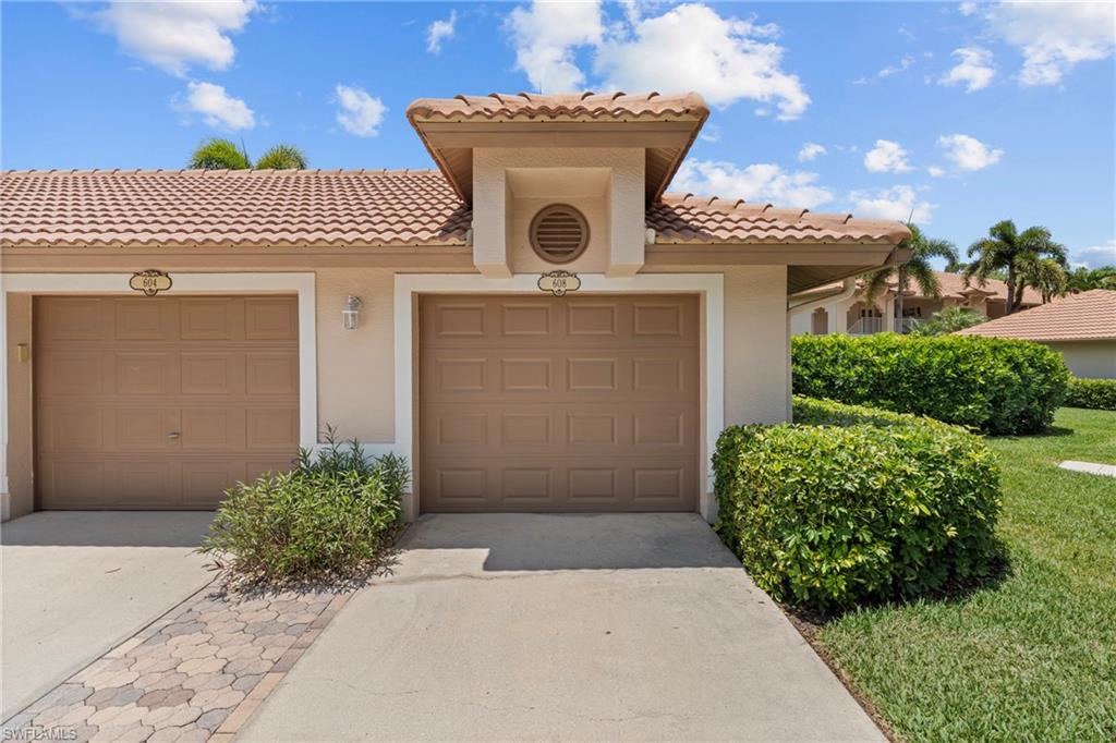 Exterior featuring a tile roof, stucco finish, two single-car garage doors, and a paver driveway