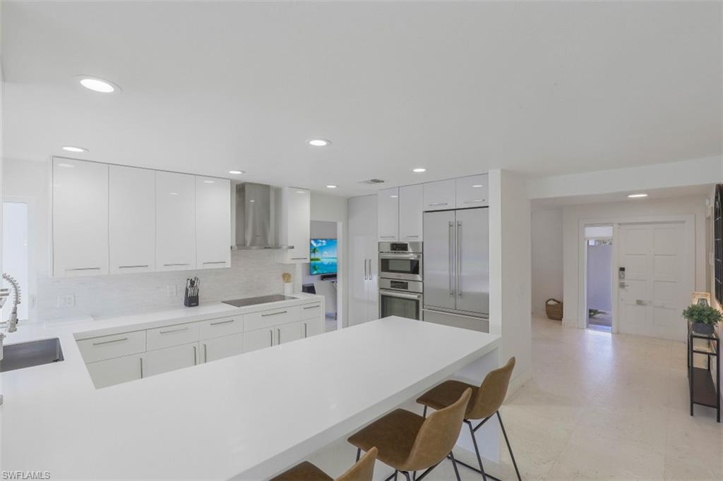 Kitchen with a peninsula, a kitchen breakfast bar, appliances with stainless steel finishes, wall chimney range hood, and recessed lighting