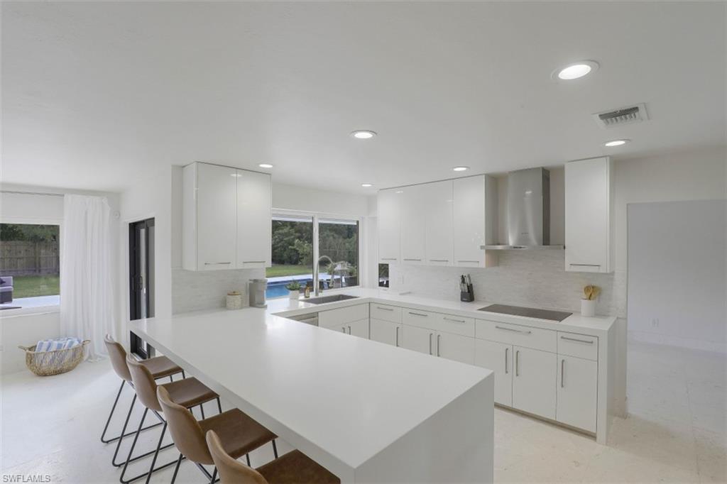 Kitchen with tasteful backsplash, wall chimney exhaust hood, white cabinetry, a peninsula, and a breakfast bar