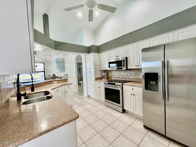 Kitchen featuring stainless steel appliances, high vaulted ceiling, white cabinetry, backsplash, and arched walkways