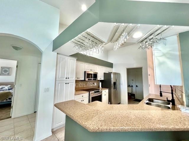 Kitchen with a peninsula, white cabinets, arched walkways, stainless steel appliances, and light stone countertops