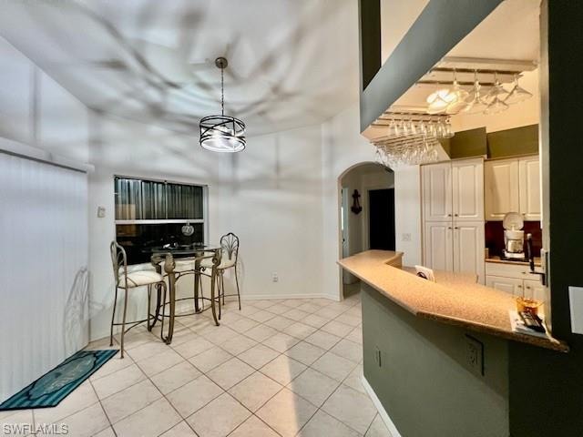 Kitchen with light tile patterned flooring, white cabinetry, arched walkways, and a kitchen bar